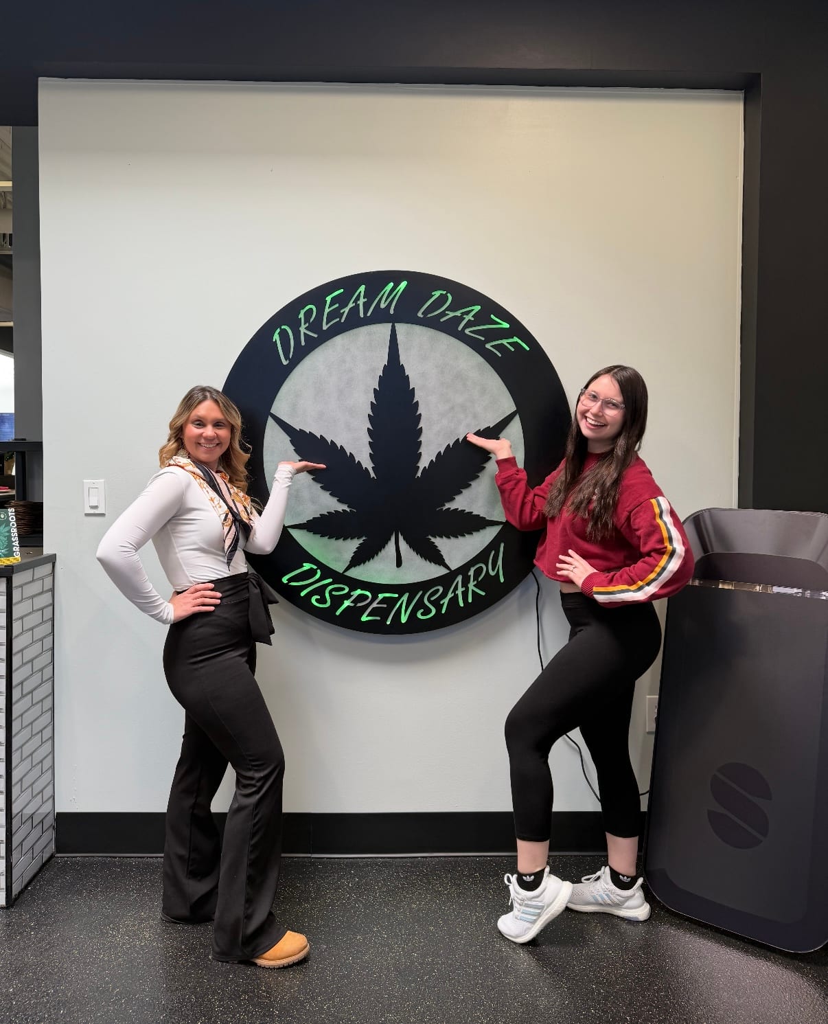 Two people by the Dream Daze Dispensary leaf logo wall in Depew
